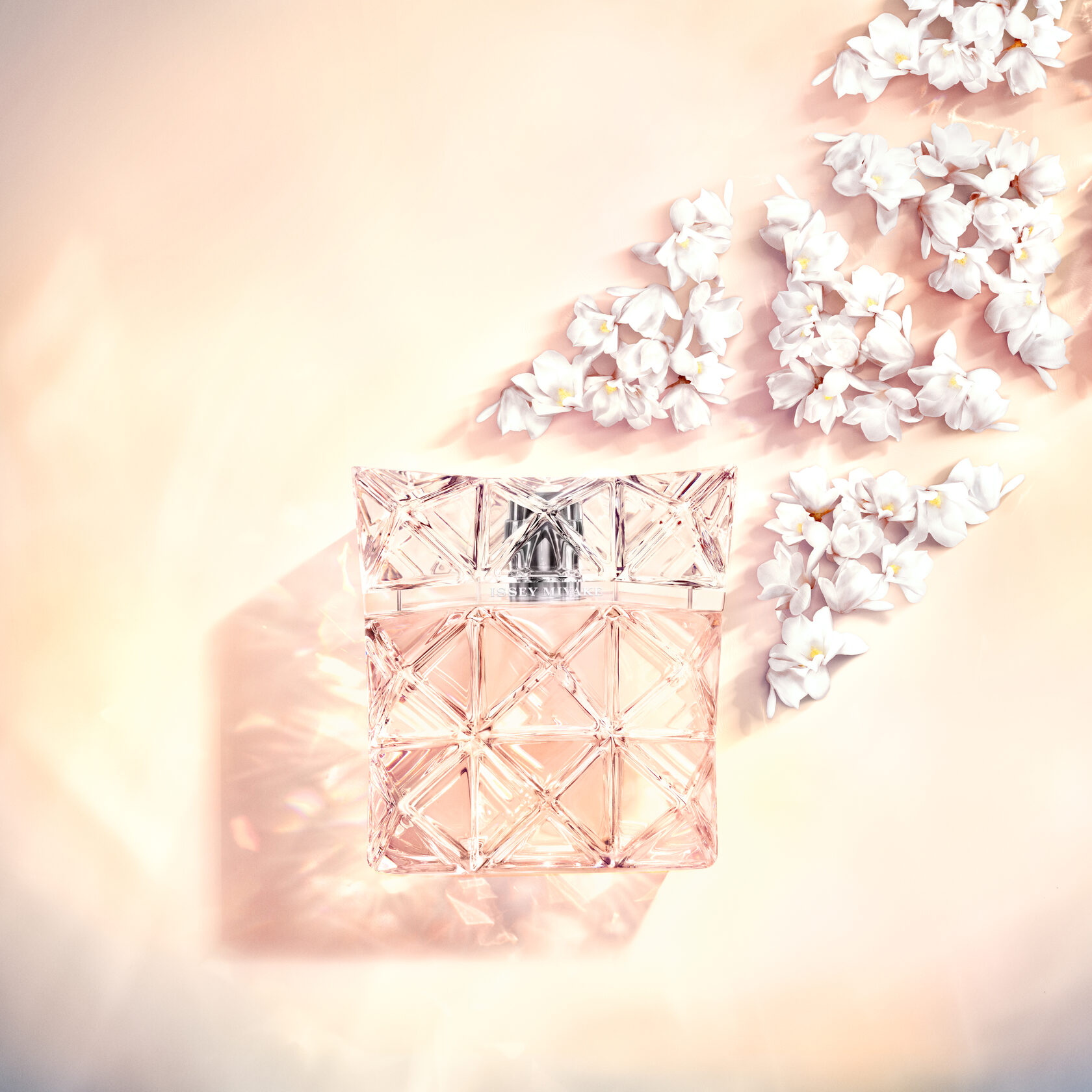 Парфюмът Lumière d’Issey от Issey Miyake, заобиколен от деликатни бели цветя на светъл пастелен фон