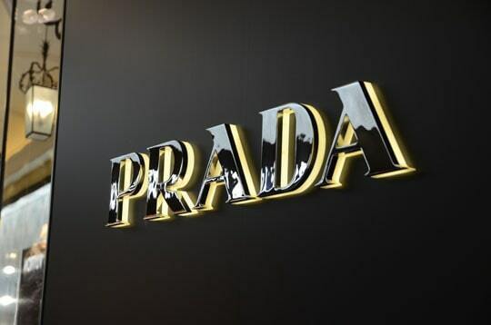 Зеркальная стальная вывеска PRADA на тёмной стене
