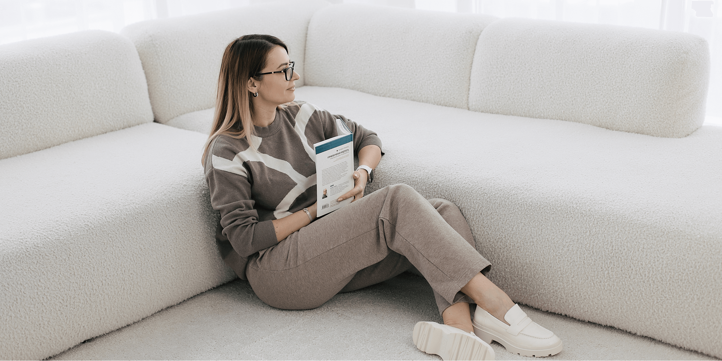 Девушка сидит на ковре возле дивана с книгой в руках