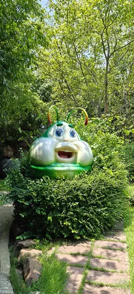 Фигура улыбающейся гусеницы среди зелени в Саду Мечты парка Dream World