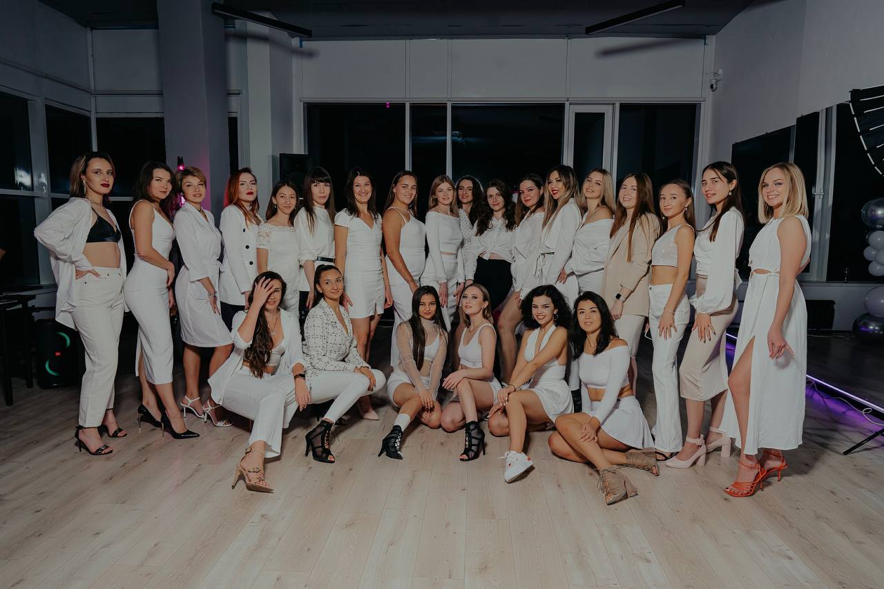 Групповая фотография участниц в светлых нарядах, позирующих в помещении студии танцев