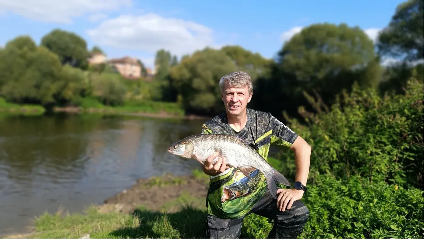 На фотографии речной водоём, на берегу припав на одно колено стоит мужчина с седыми волосами. держит в руке очень крупну рыбу жереха
