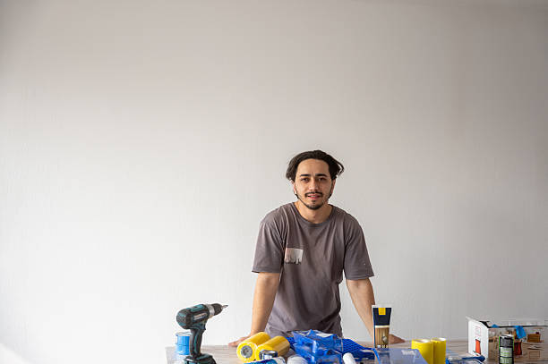 Handyman preparing for home renovation project with tools and materials Young handyman standing confidently behind a table with various tools and materials, ready to start a home renovation project drywall Repairs Handyman Services stock pictures, royalty-free photos & images