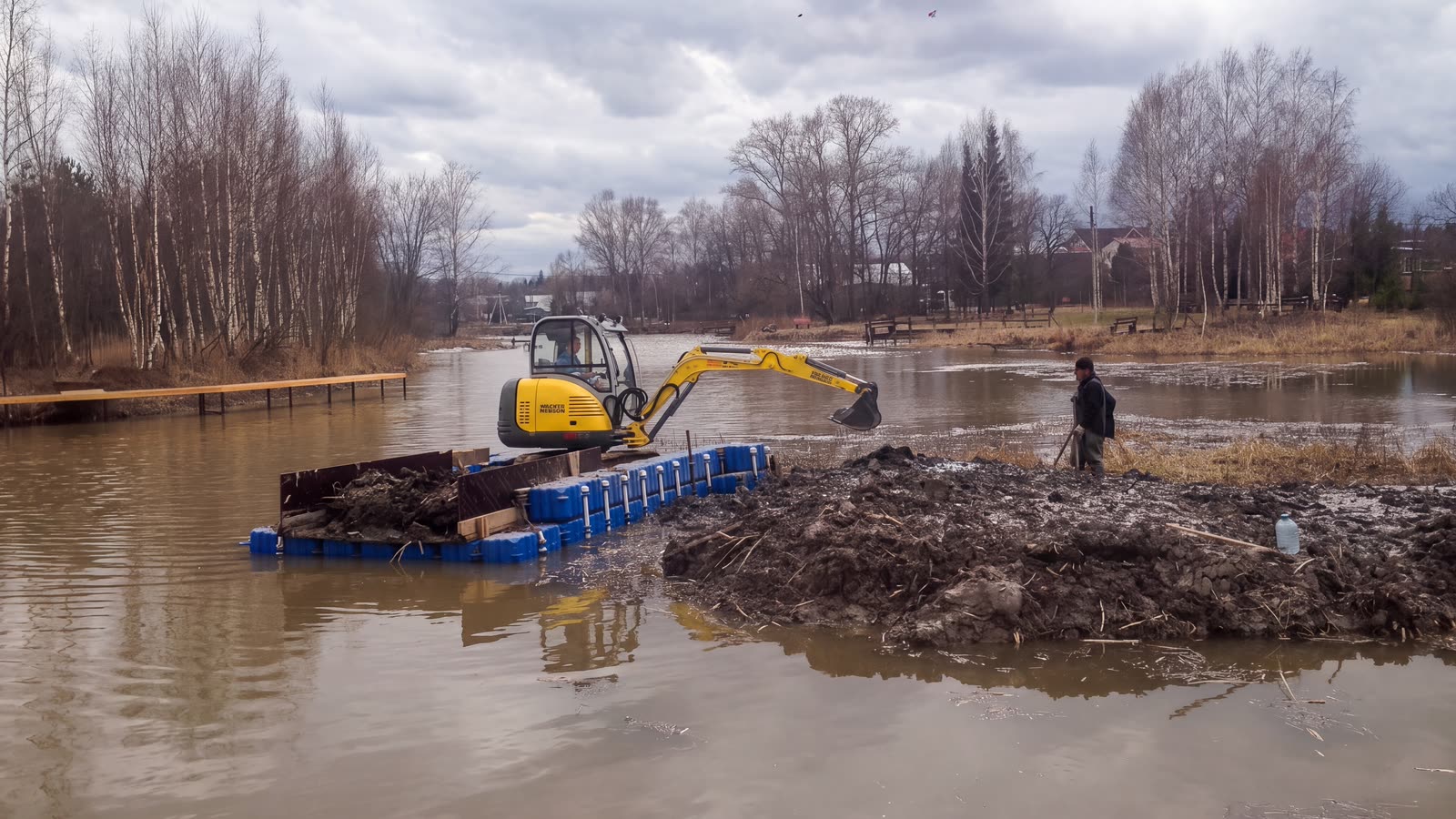 Экскаватор на понтонах вынимает грунт со дна водоема
