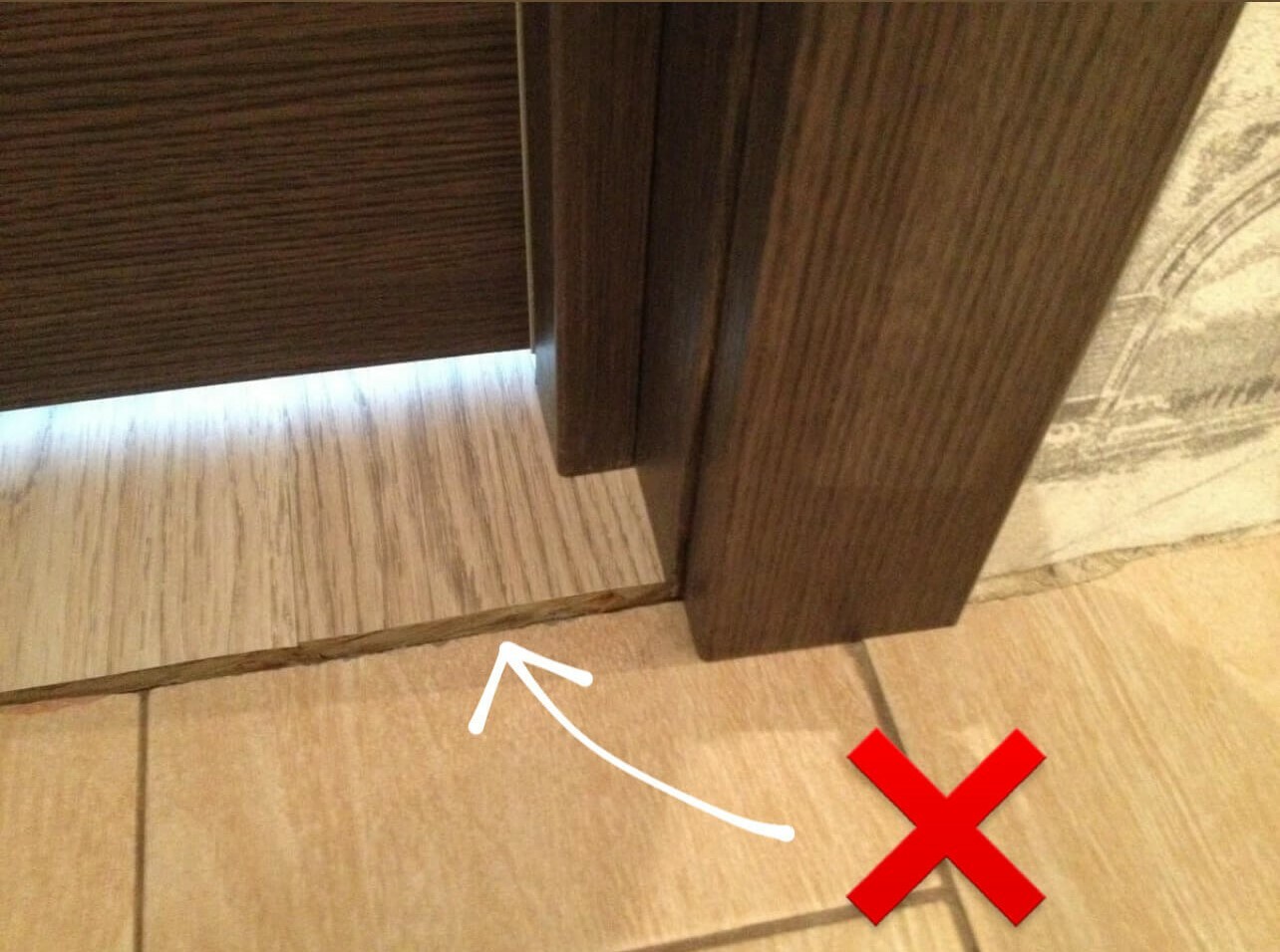 Неправильный стык напольных покрытий под дверью.