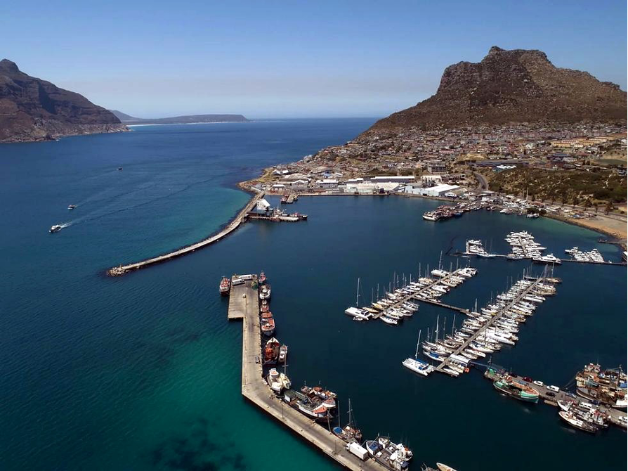 Hout Bay Harbour крупнее: рядом стоят яхты и рабочие рыбацкие суда — без попытки изображать глянцевый курорт