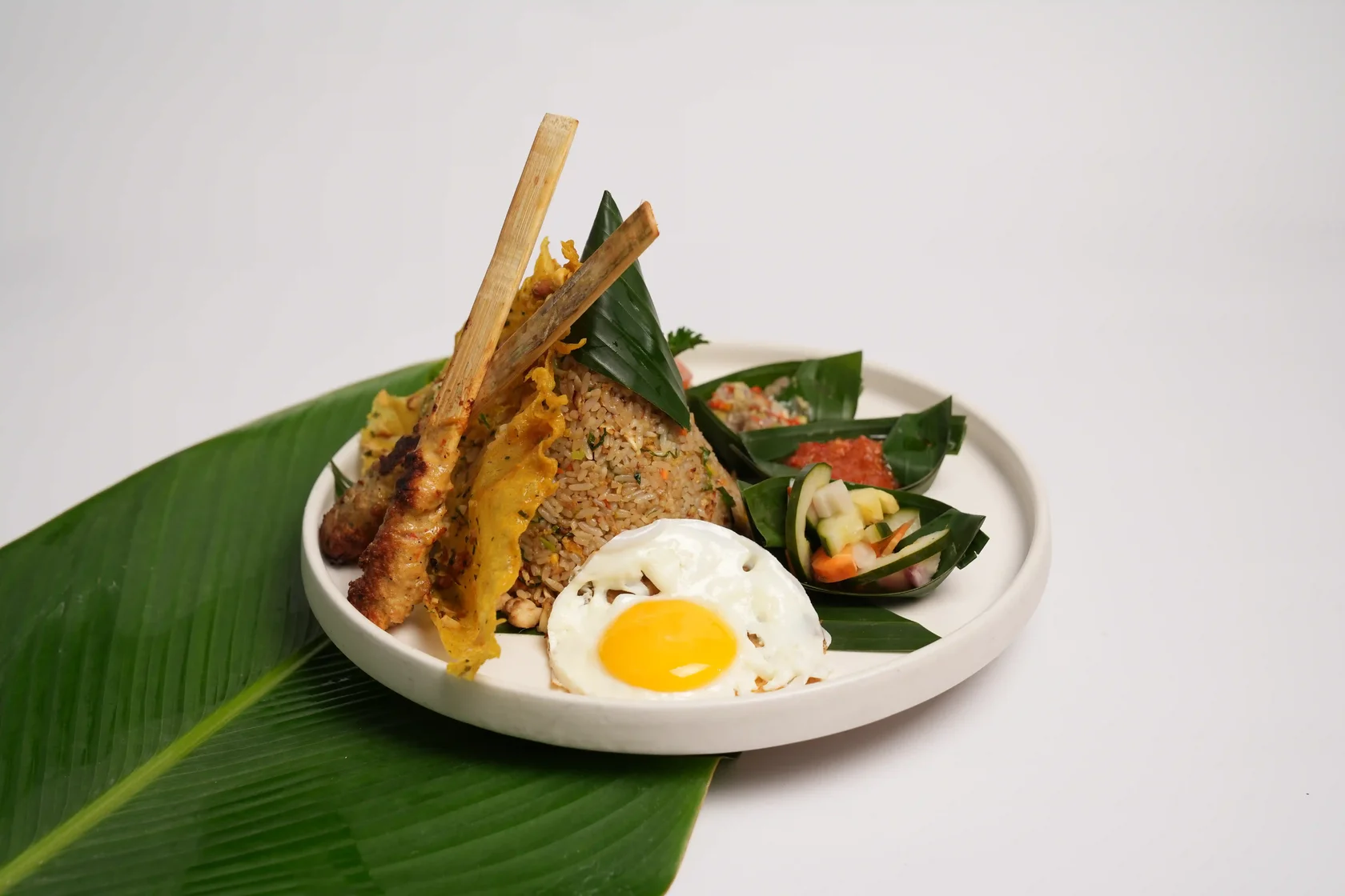 Indonesian nasi goreng served with a sunny-side-up egg, chicken satay, crackers, pickles, and sambal