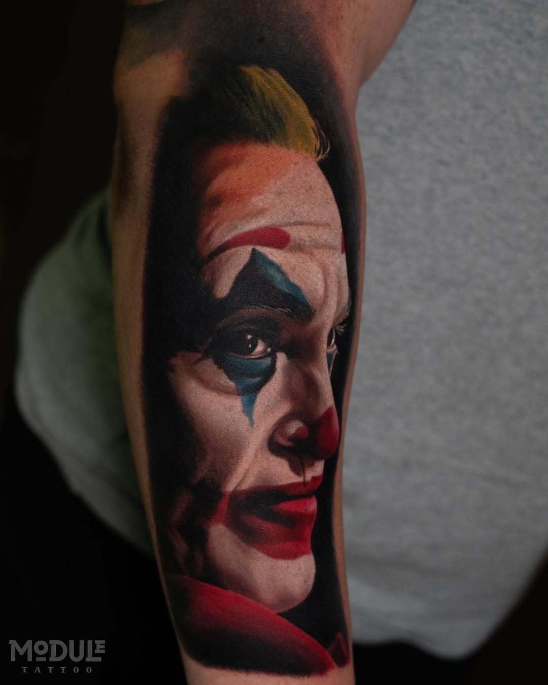 High-contrast hyper-realistic portrait tattoo of Joaquin Phoenix as the Joker on an arm, featuring detailed skin texture and vibrant movie makeup colors, by Rinat Mingazdinov, Los Angeles
