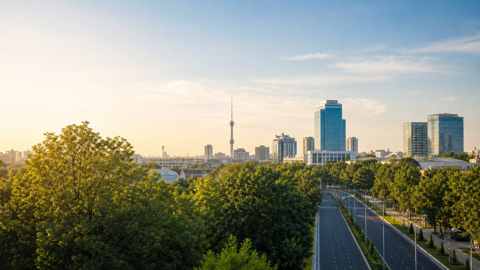 Tashkent skyline with modern buildings and a television tower above a tree-lined avenue in warm evening light