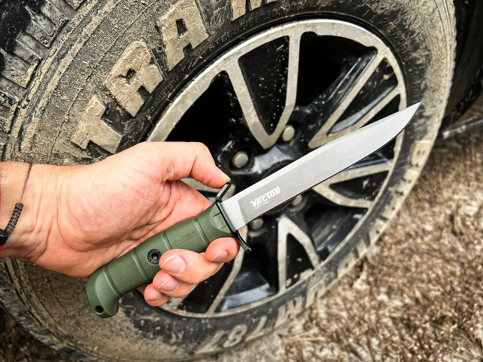 Olive Kizlyar Supreme Vector held securely beside an off-road tyre