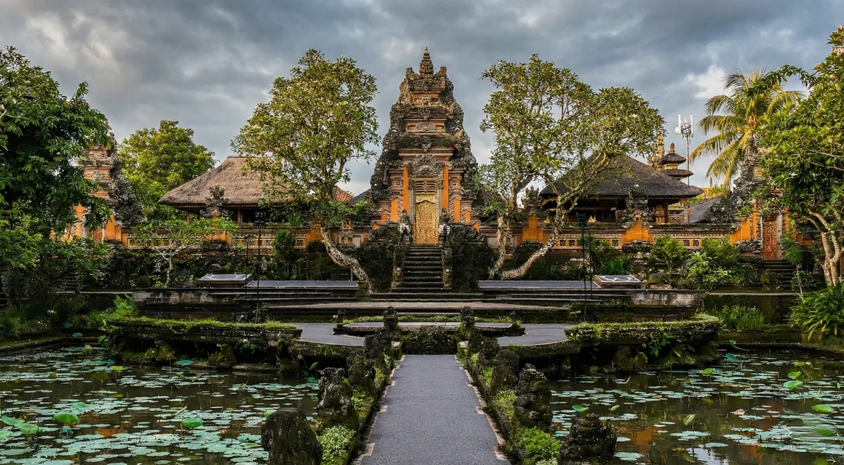 Ubud Palace exterior view with traditional Balinese architecture, stone gates, lotus pond, and lush gardens in the heart of Ubud Bali