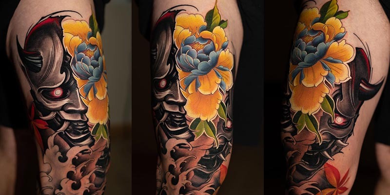 Japanese  demon mask tattoo on thigh with glowing red eye and peony flower outlines in realism style