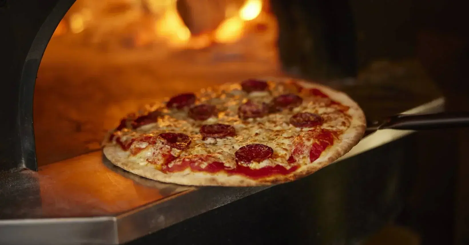 A classic pepperoni pizza coming fresh out of a traditional wood-fired oven, highlighting the best pizza in Ubud.