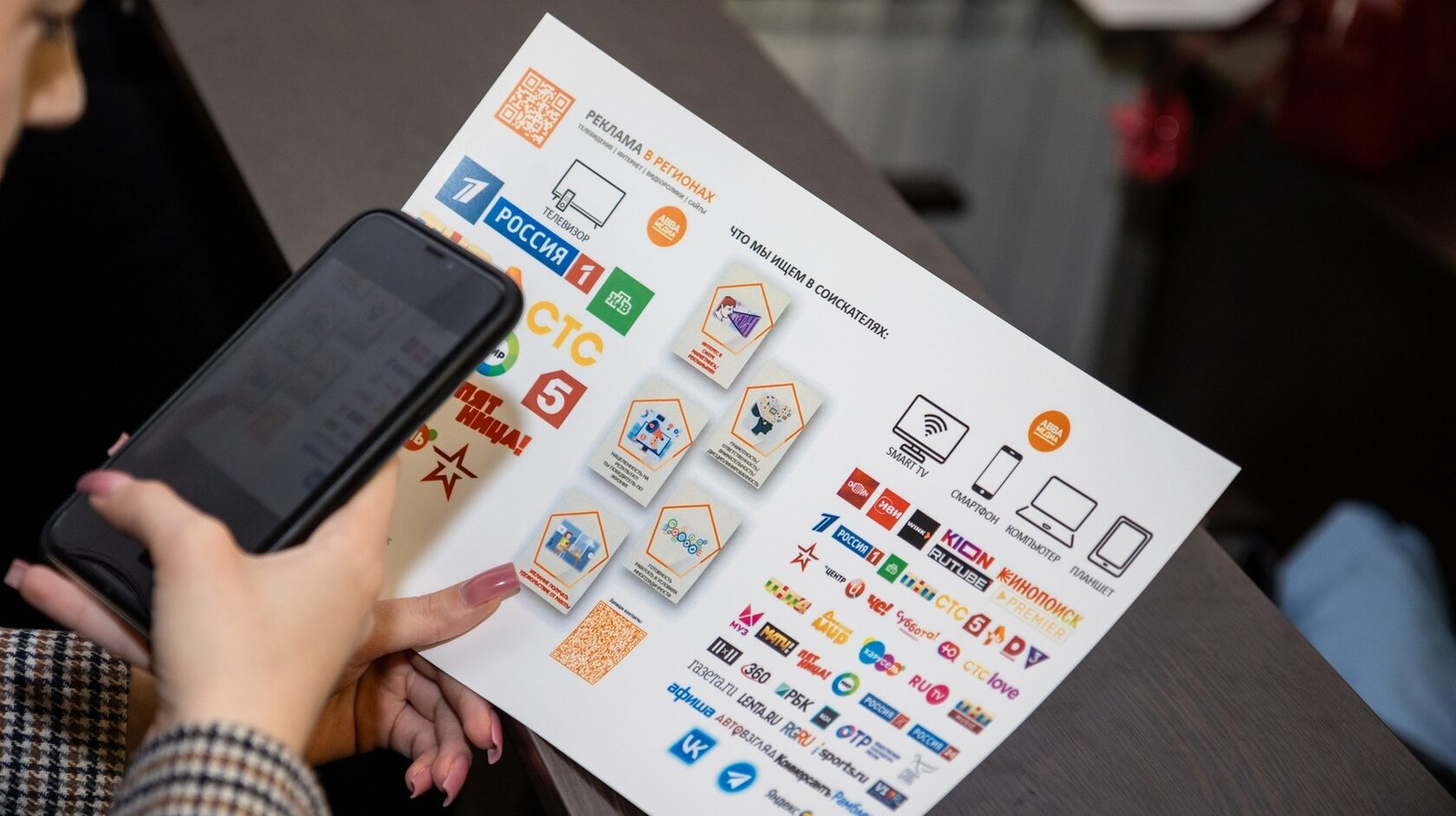 Участница держит смартфон и листовку с QR-кодом о рекламе в регионах