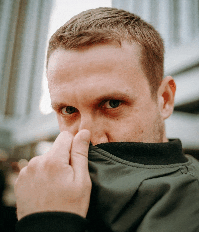 Ваня прикрывает половину лица воротом куртки и смотрит в камеру