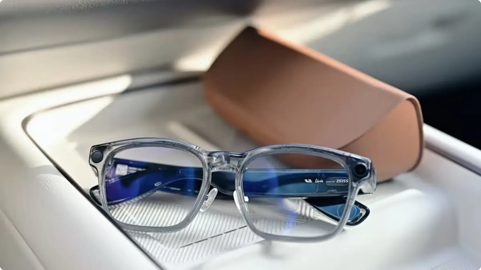 Умные очки Li Auto Livis в прозрачной оправе с линзами Zeiss и встроенными камерами на заушниках, лежат на белой ребристой панели рядом с коричневым кожаным чехлом.