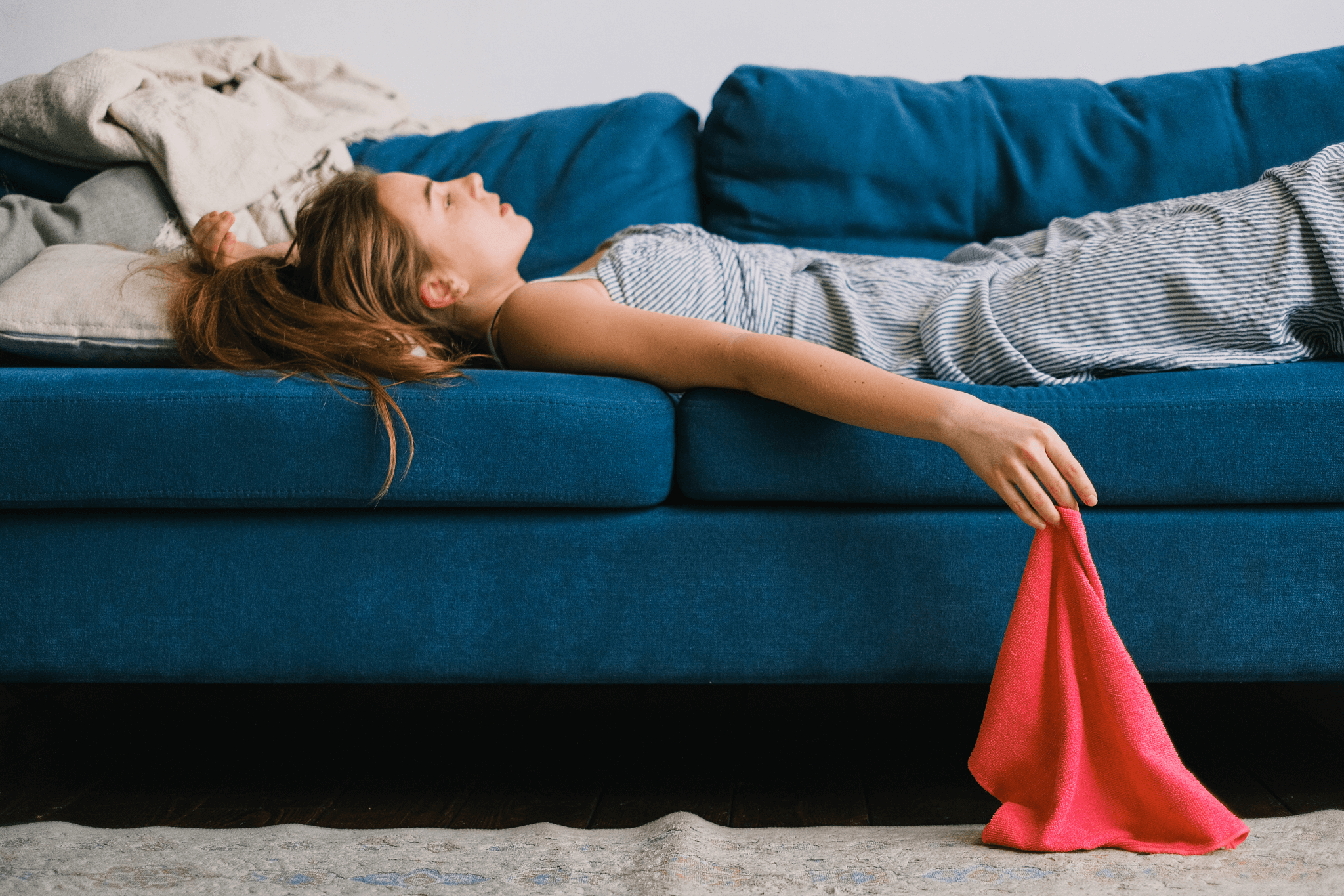 Erschöpft wirkende junge Frau liegt tagsüber in Alltagskleidung auf einem Sofa