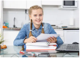 Photo 2 — Улыбающаяся девочка сидит за кухонным столом с тетрадками, учебниками и ноутбуком