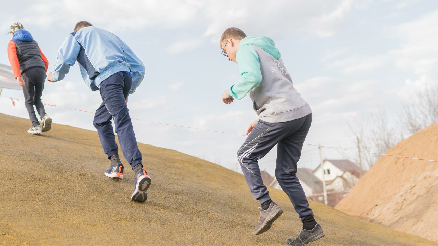 Ваня в белой футболке, зеленой куртке и синих джинсах перепрыгивает через перила лестницы