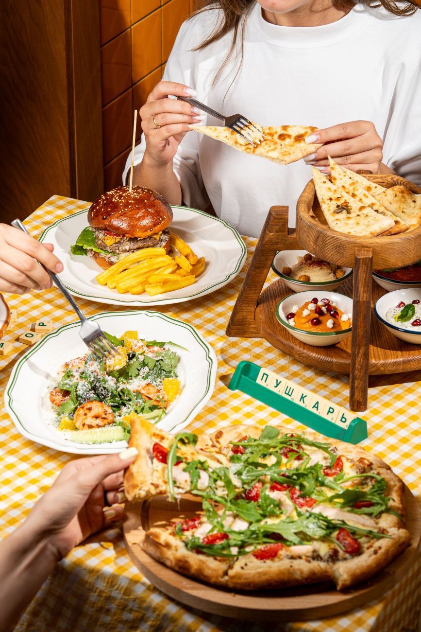 Гостья за столом с пиццей, бургером и лепёшками
