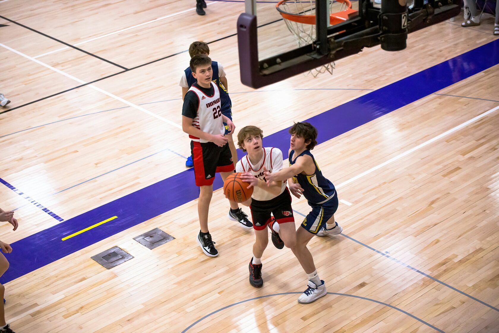 Юные баскетболисты в яркой форме в динамичном моменте игры в современном зале. Момент броска мяча в кольцо.