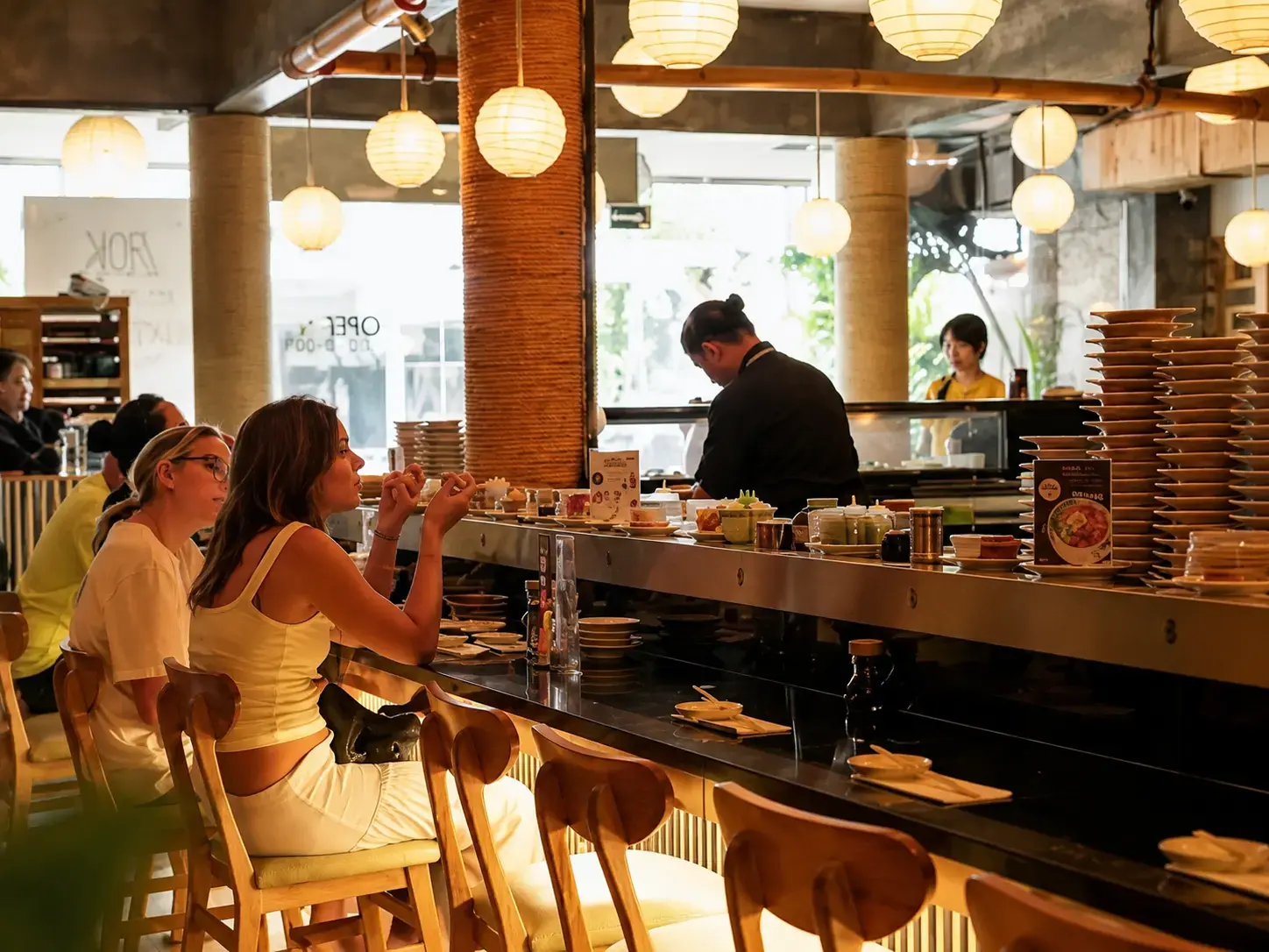 A casual lunch scene inside Sushimi Seminyak, with customers dining at the active sushi train counter. Great for a quick, fuss-free meal.