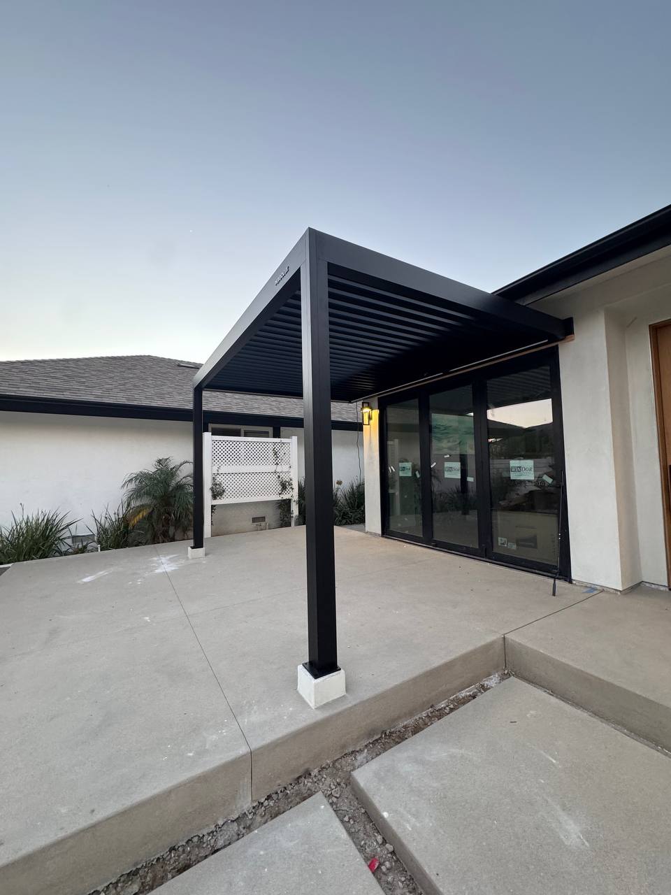 Wide corner view of the completed black pergola on concrete support bases.