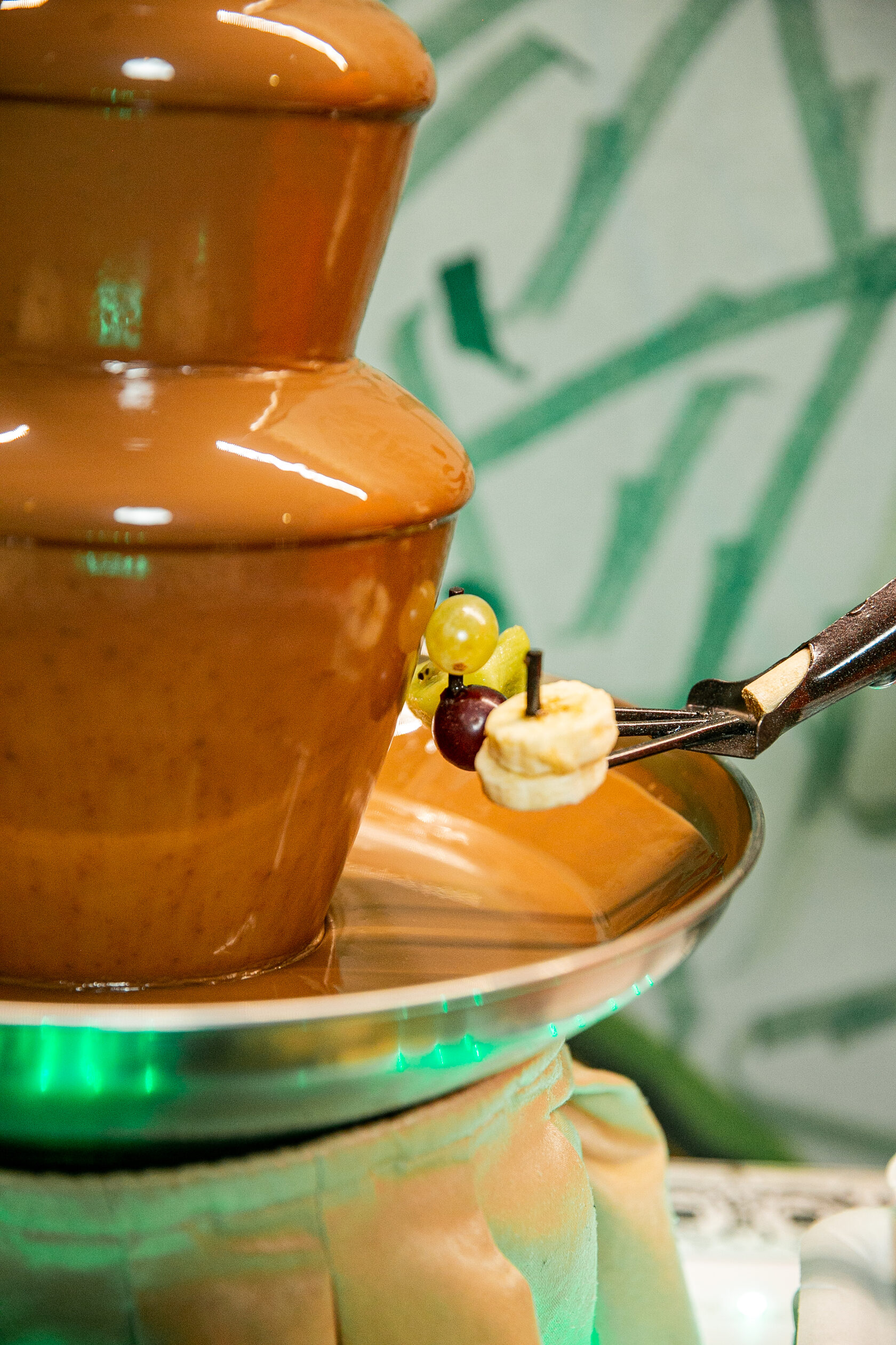 Шоколадный фонтан крупным планом размером 50 см, вокруг которого на шпажке нарезанные дольками бананы, подходящие для погружения в шоколадную кастрюлю.
