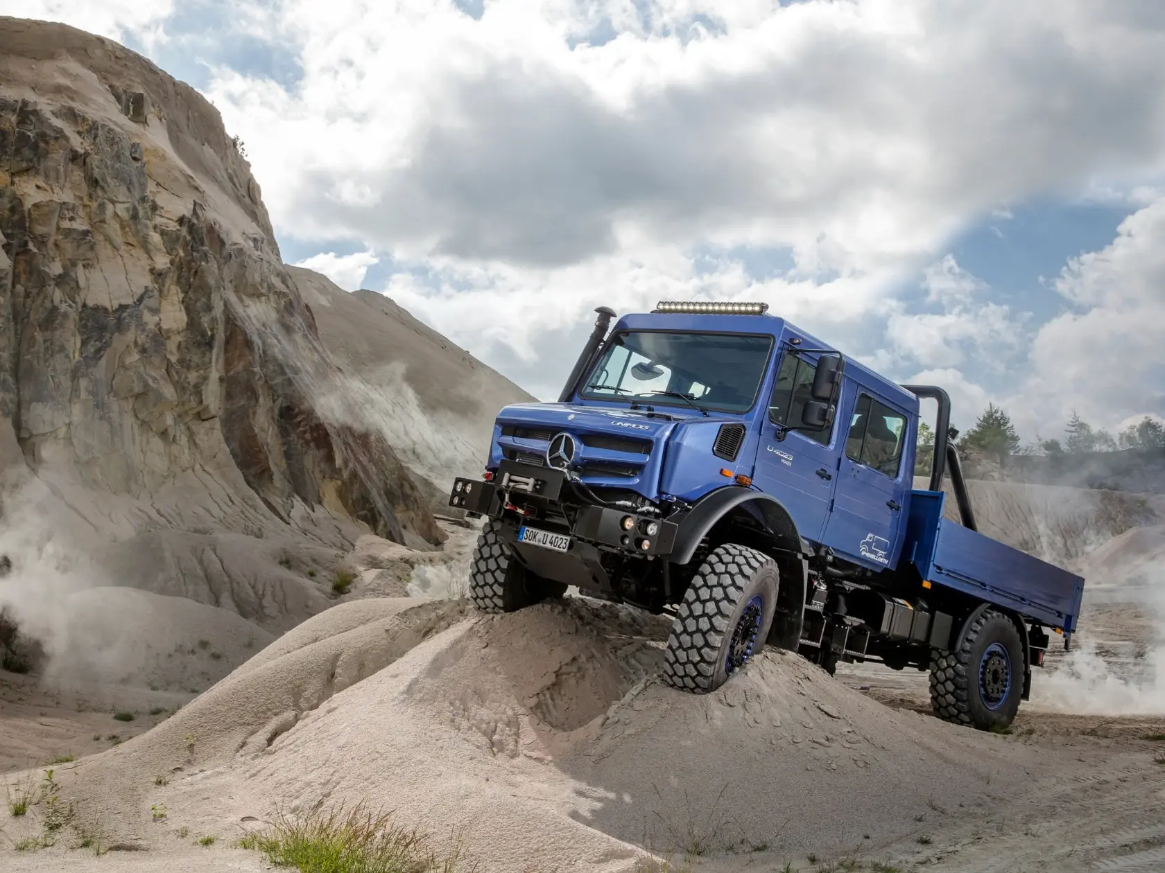 Синий Unimog поднимается на крутую песчаную дюну