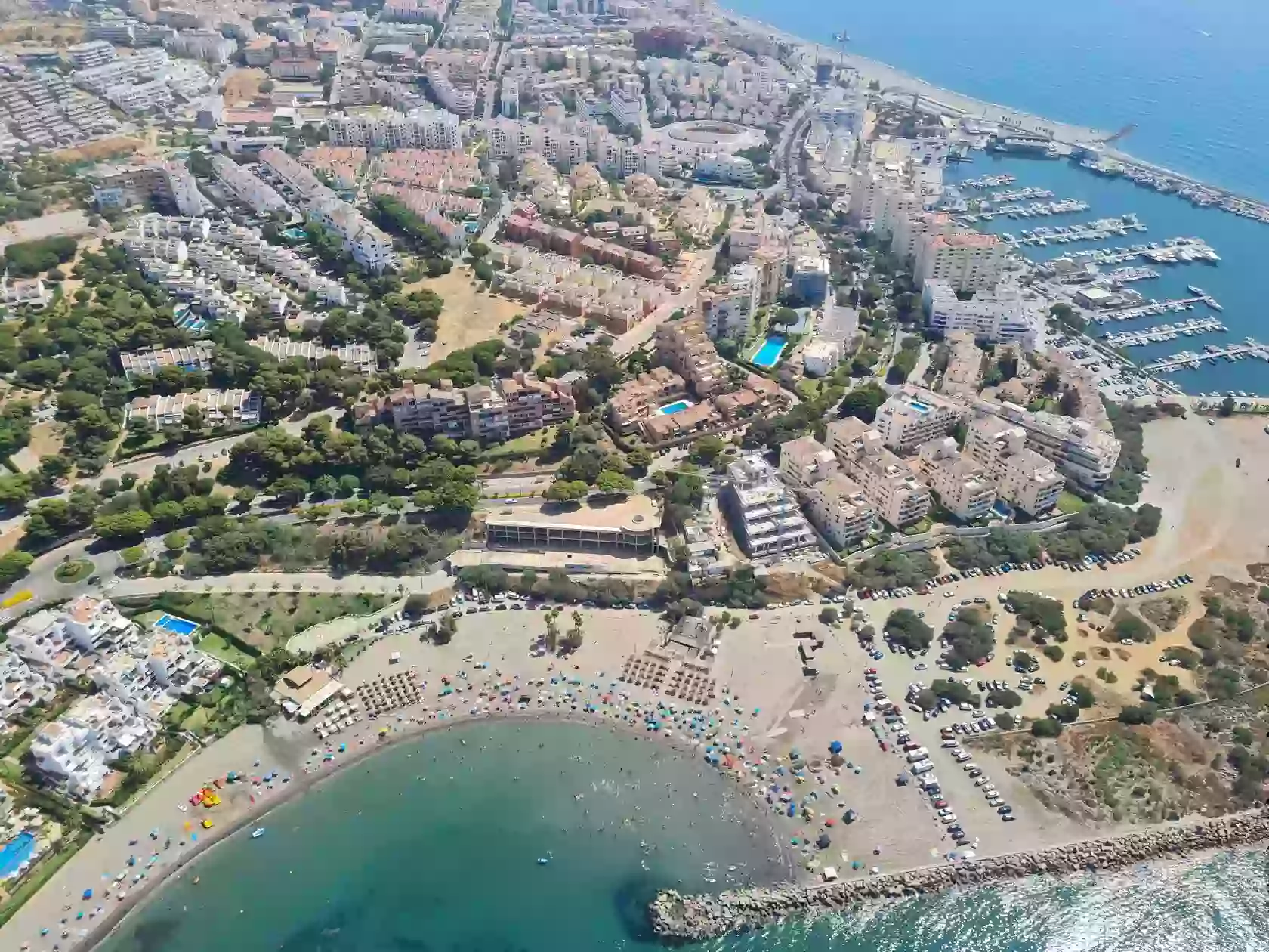 A tranquil beach in Estepona, Spain, featuring golden sands, crystal-clear turquoise waters, and a scenic backdrop of lush palm trees and mountains under a vibrant blue sky.