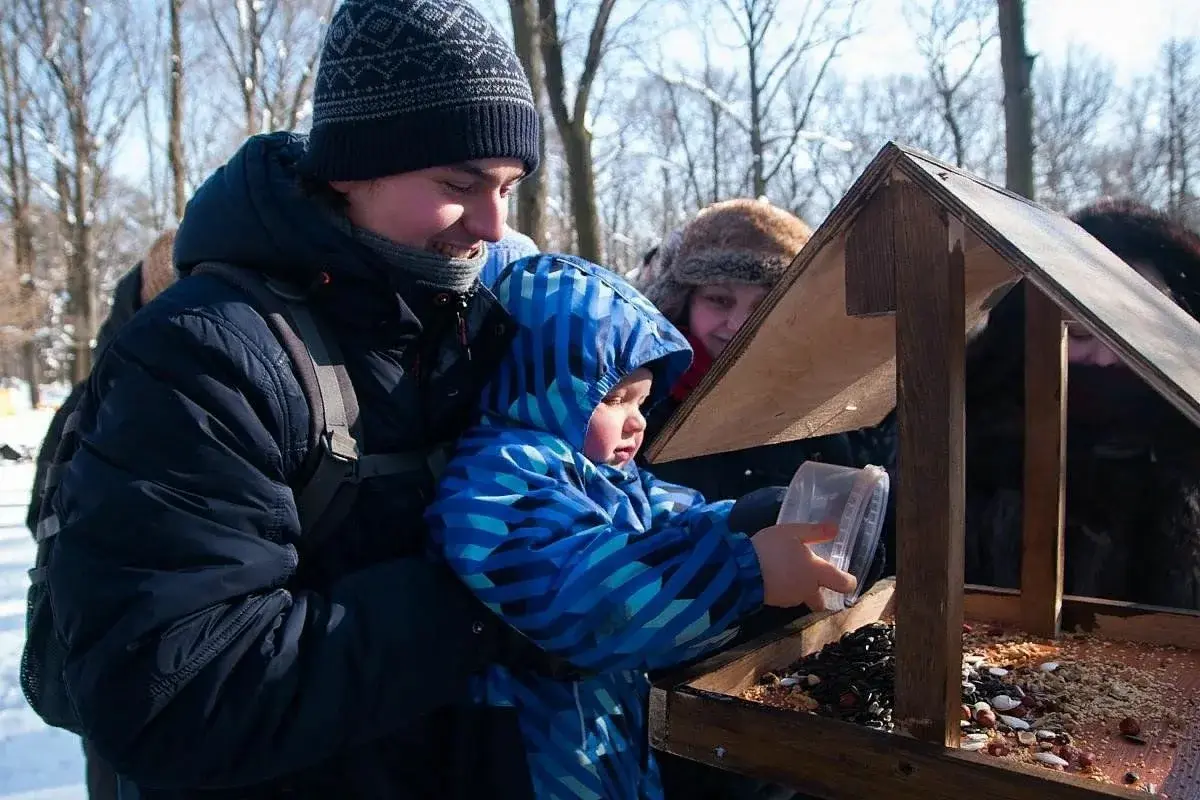 Семья, отец и дочь, вешают деревянную кормушку для синиц и зимующих птиц в парке 12 ноября.