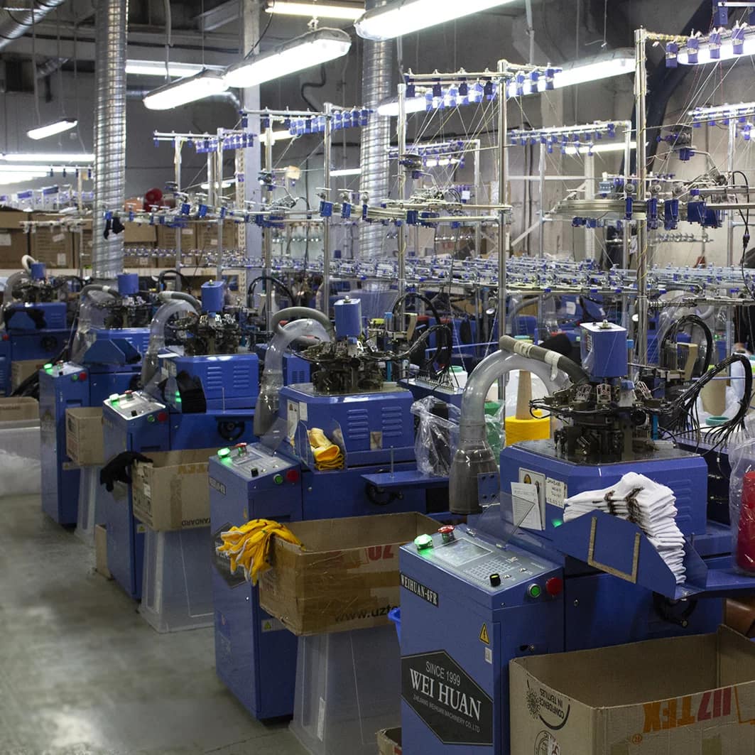 Свой завод носков в СПБ. Чулочно-носочный завод фото. Много носочных станков в один ряд. Синие станки для носков на фабрике. Свое производство носков.