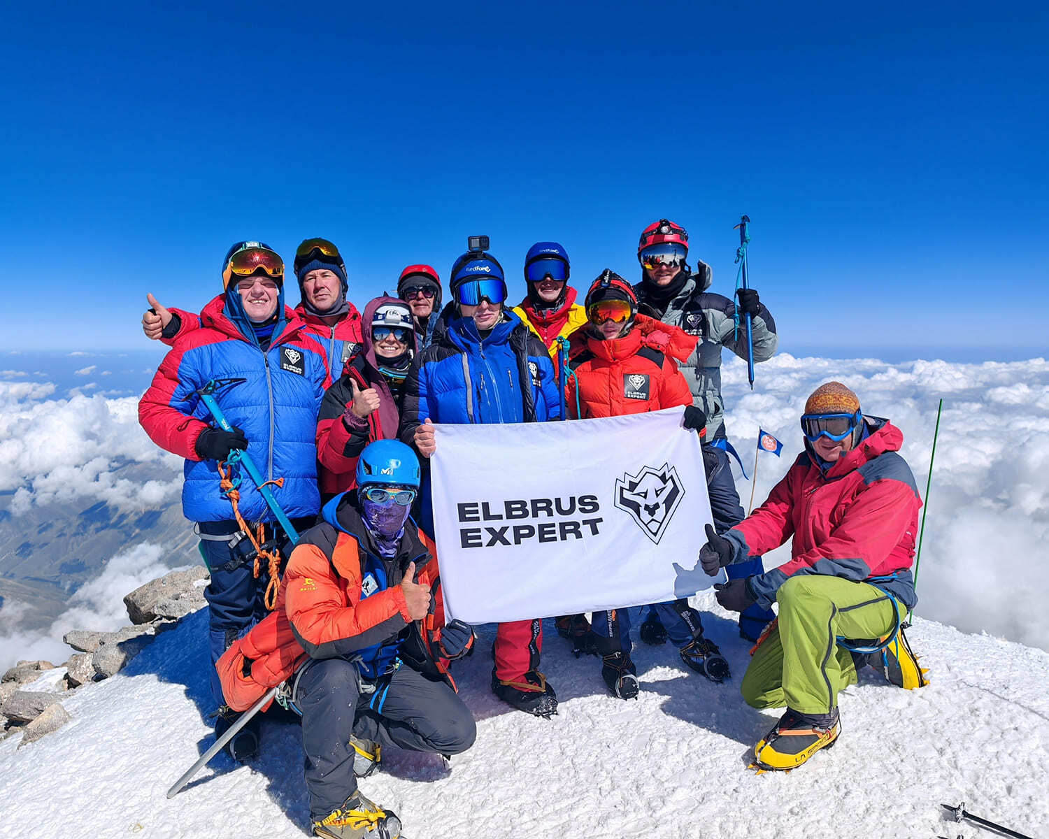 Elbrus Expert team with the company flag on the summit of Elbrus above the clouds