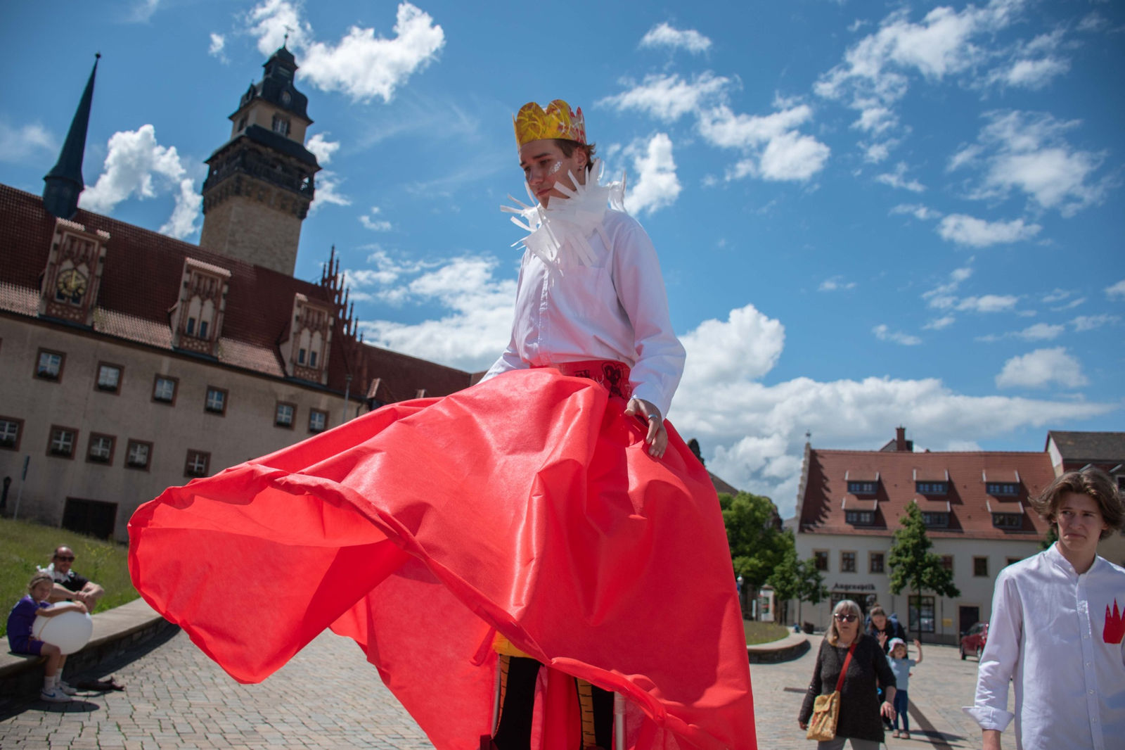 A king on stilts in a red skirt in front of the castle