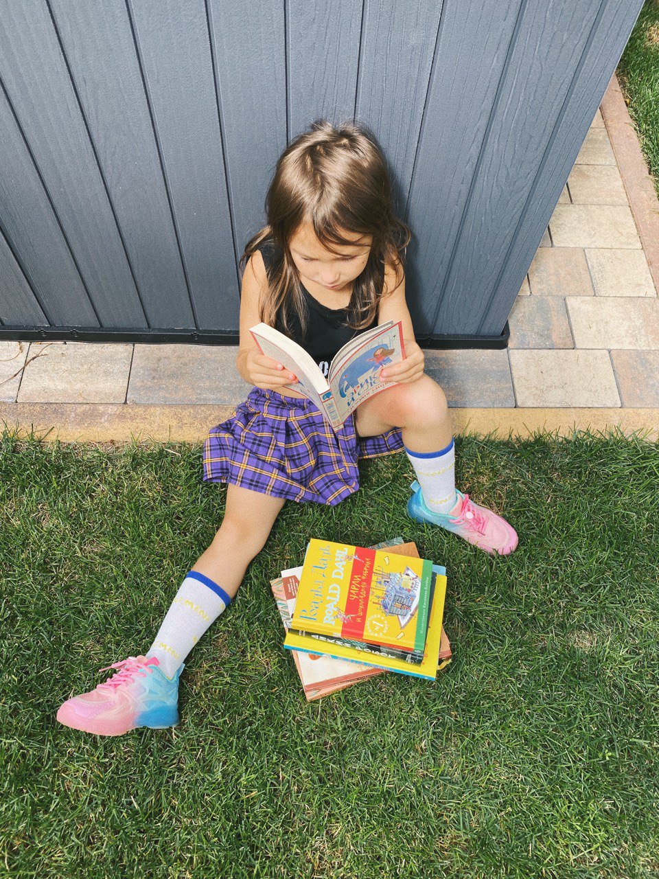 Девочка в юбке сидит на траве с книгами и читает