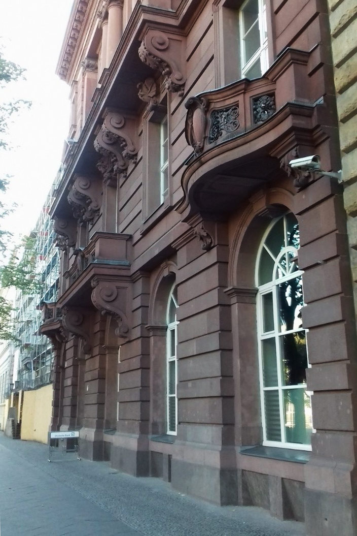 Тифлокомментарий. Цветная фотография. Фасад четырехэтажного здания в неоклассическом стиле темно-розового цвета. На первом этаже пластиковые арочные окна. Фасад украшен объемными балконами с кованым декором и колоннами. Это современный вид здания в центре Берлина, в котором с 1951 по 1991 находился Секретариат федерации.