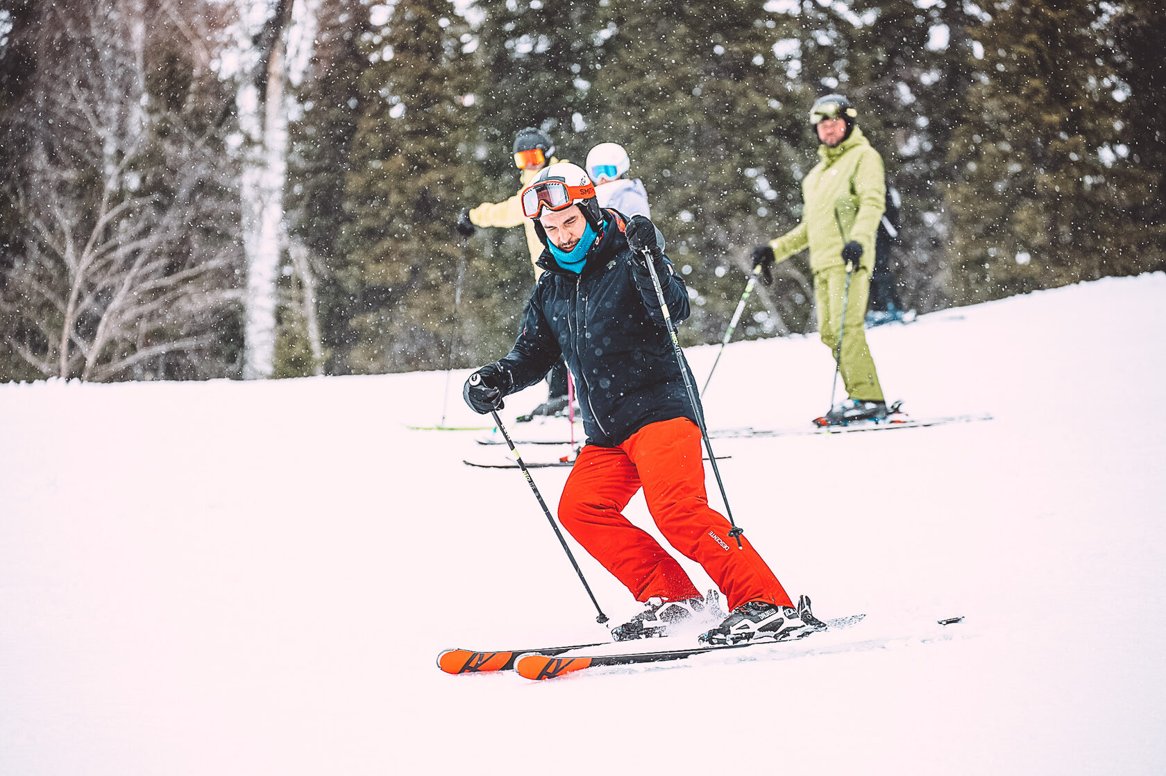 Профессиональный инструктор по горным лыжам в процессе обучения учеников показывает упражнение на торможение