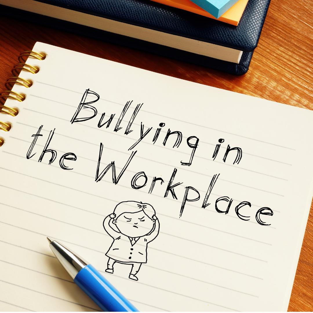 Words bullying in the workplace written on notebook paper with person sketched below it and blue pen laying on page