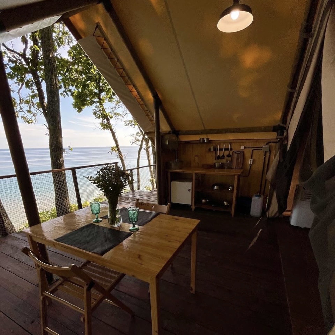 Вид на террасу глэмпинга. Кухонные принадлежности, бак для воды, умывальник, стол и стулья.