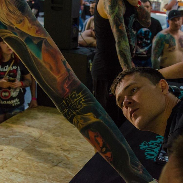 A high-quality full-sleeve color realism tattoo featuring Star Wars characters, including Darth Maul and the iconic movie logo, being showcased by the artist at a tattoo convention, jury member Rinat Tattarin Mingazdinov