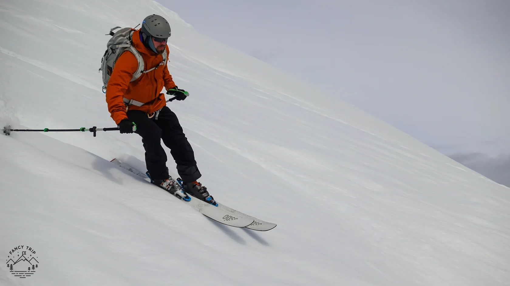 A skier descends a pristine Antarctic snow slope during a ski-touring expedition carving smooth turns through untouched powder. Wearing a helmet backpack and technical alpine gear the skier navigates the remote mountains with no trails or ski lifts in sig