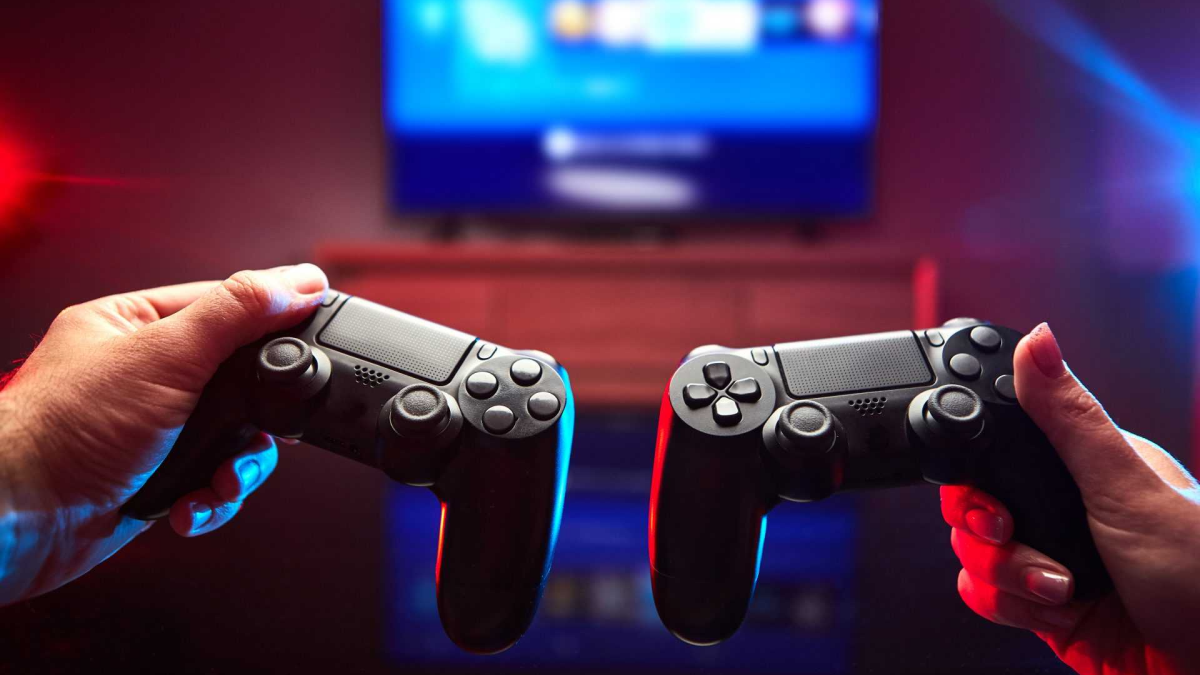 Геймпады в руках у пары на фоне экрана с включенной приставкой
