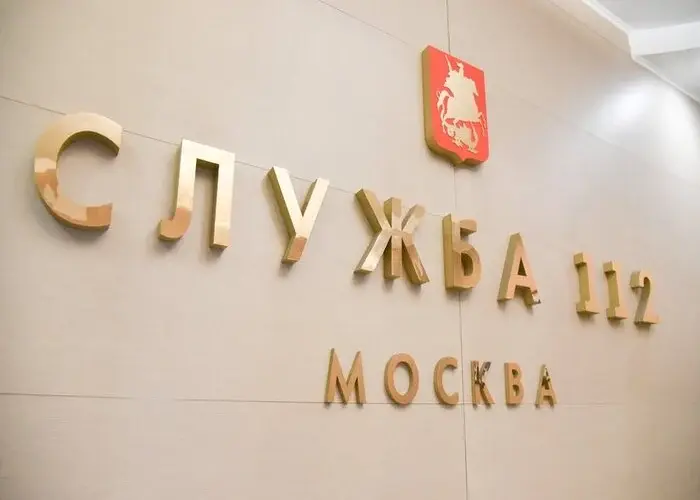 Латунная надпись Служба 112 Москва на светлой интерьерной стене
