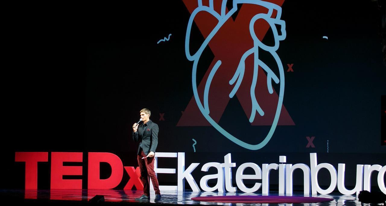 Ведущий с микрофоном на сцене с крупной надписью TEDxEkaterinburg