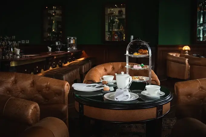 A luxurious top dinner in Ubud setting with a roaring twenties aesthetic, featuring classic leather armchairs and a multi-tiered stand of elegant light bites ready to be enjoyed.