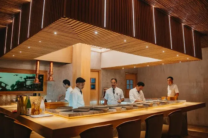 The polished omakase counter at Takumi, where chefs prepare a premium Japanese dining experience under modern wooden ceiling lights. One of the top spots for high-end sushi in Seminyak.