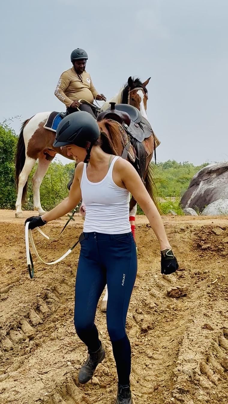 Horseback rider at Vonfidel Ranch walking beside a saddled horse through dry tropical terrain in Sri Lanka, reflecting the Ranch’s calm, low-volume and welfare-first riding philosophy.