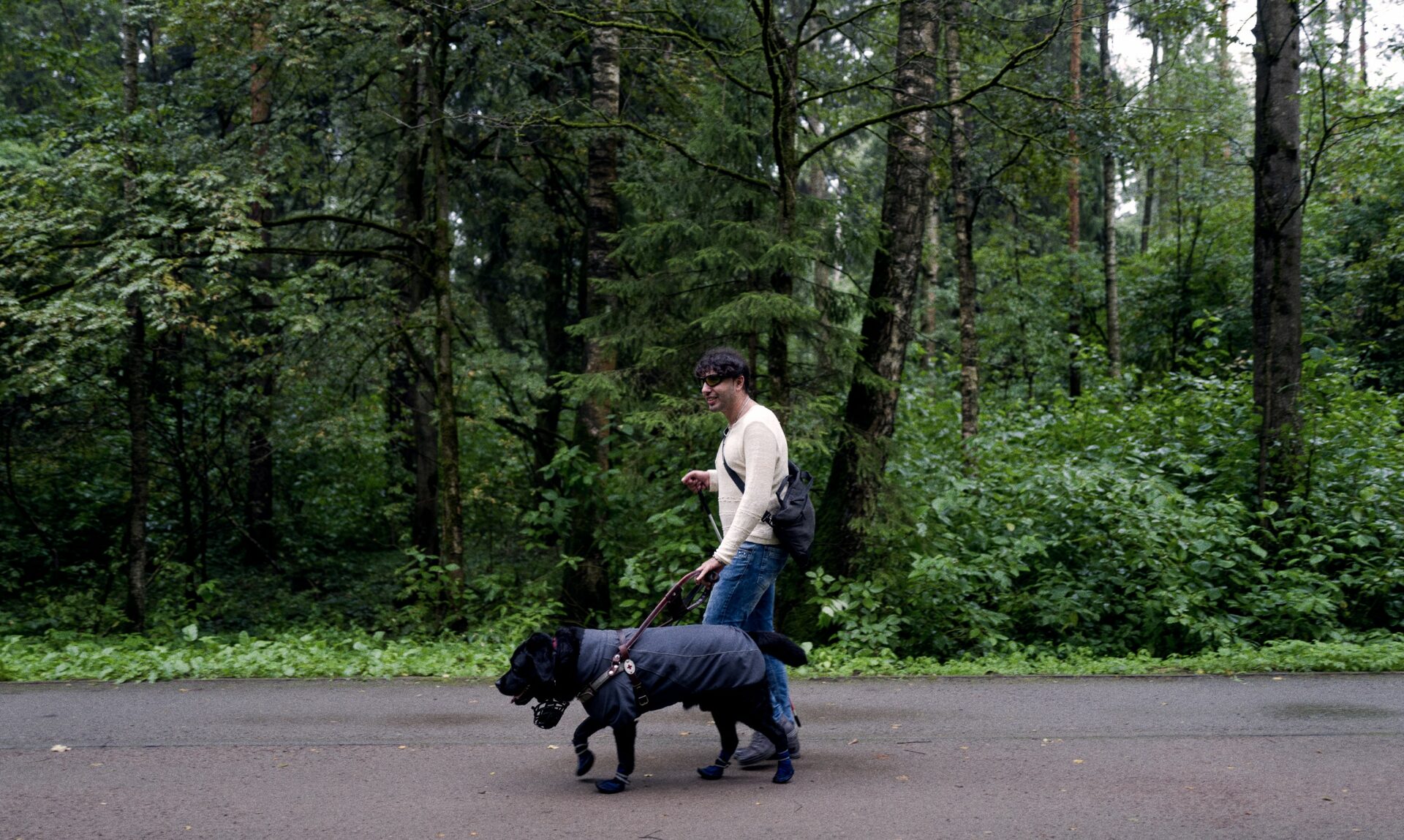 Руслан вместе с собакой-поводырём идёт по дороге посреди леса