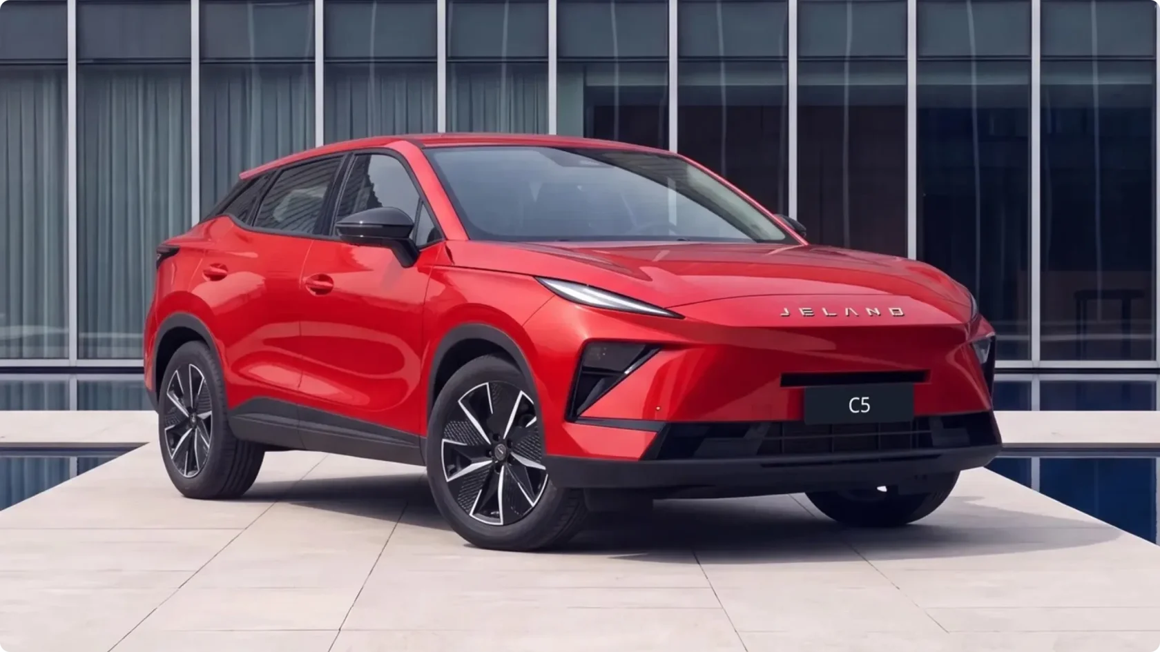 Красный автомобиль JELAND C5 — современный городской кроссовер перед стеклянным офисным зданием.