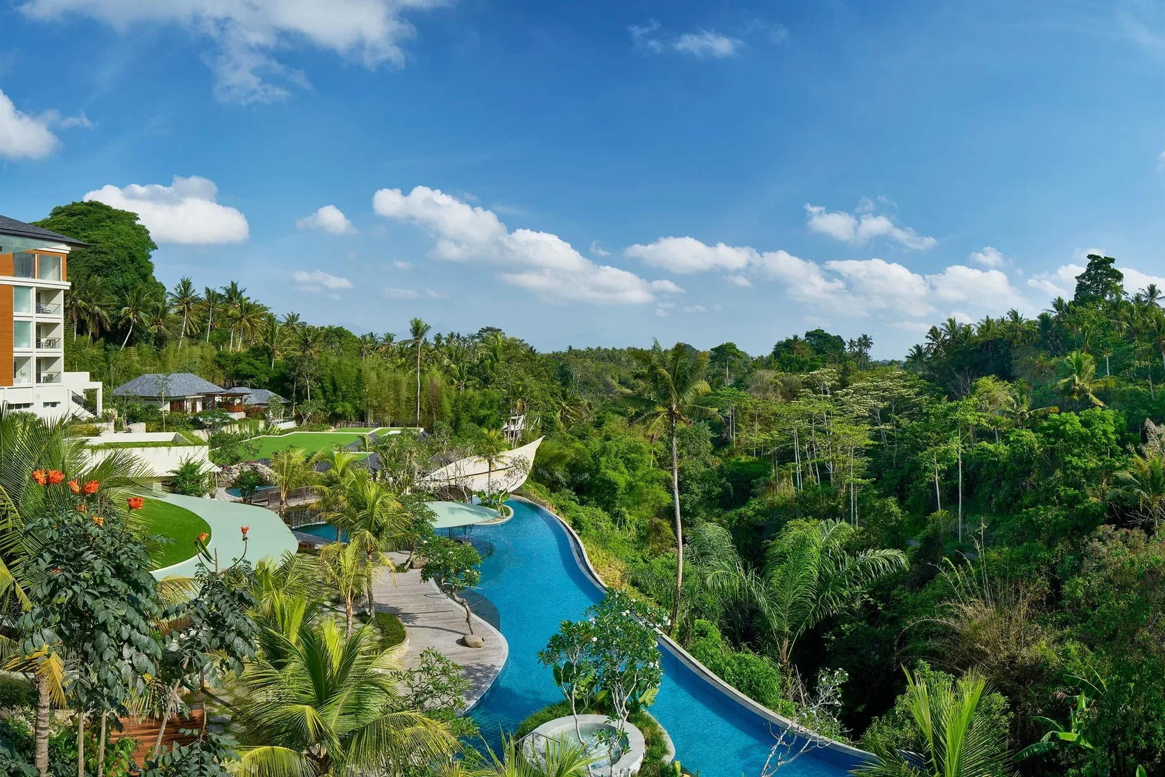 Expansive curving swimming pool and modern resort amenities nestled into the dense, vibrant jungle canopy at The Westin Resort & Spa Ubud Bali.